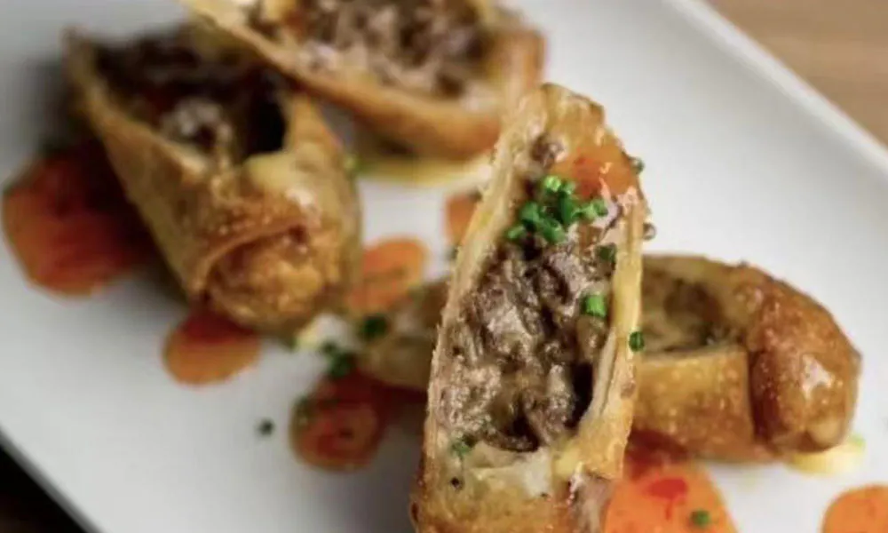 Beef-filled fried spring rolls with sauce drizzle and chive garnish